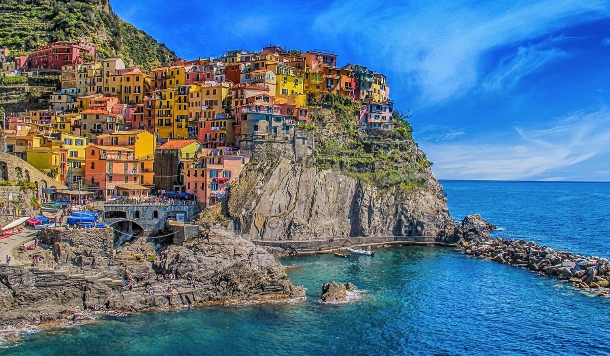 Scenic view of Manarola, a picturesque coastal village in Cinque Terre, Italy, with colorful houses perched on a cliff overlooking the blue Mediterranean Sea under a bright sky.